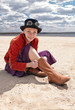 Girl wearing boots and danger style glasses sitting on beach