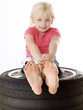 Foto: Cute blond girl sitting on summer tyre with a toy car Cute blond girl sitting on summer tyre with a toy car