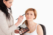 Cute blond-haired woman having her make up done by a make up art