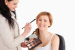 Attractive blond-haired woman having her make up done by a make