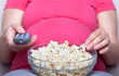 Pregnant woman sit and eat popcorn on sofa, watching television Pregnant woman sit and eat popcorn on sofa, watching television