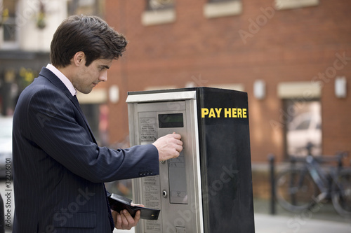 Photo: A businessman putting coins in a parking meter A businessman putting coins in a parking meter