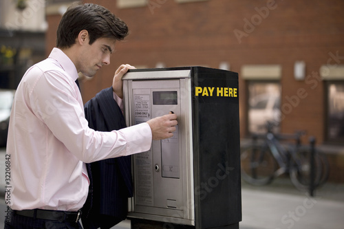 Photo: A businessman putting coins in a parking meter A businessman putting coins in a parking meter
