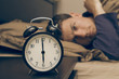 Alarm clock with male model in bed in background.