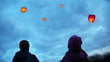 boy and girl look on flying chinese lanternes highly in sky