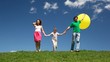 family of three holding yellow bubble hands down hill with grass