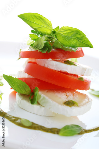 Photo: Fresh salad with goat cheese, tomato and basil pesto on a white Fresh salad with goat cheese, tomato and basil pesto on a white