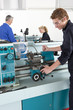 Teacher talking to students using lathe in vocational school