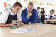 Teacher watching student using soldering iron in vocational school