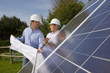Technicians holding blueprints talking near large solar panels