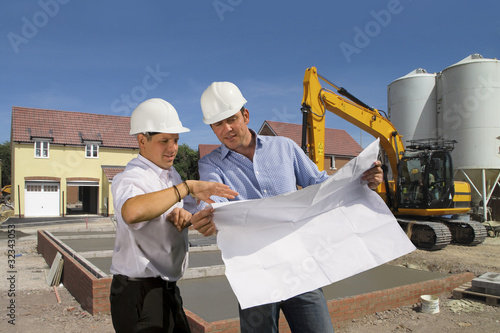 Photo: Construction workers holding blueprints talking on construction site Construction workers holding blueprints talking on construction site