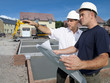 Photo : Construction workers holding blueprints talking on construction site Construction workers holding blueprints talking on construction site