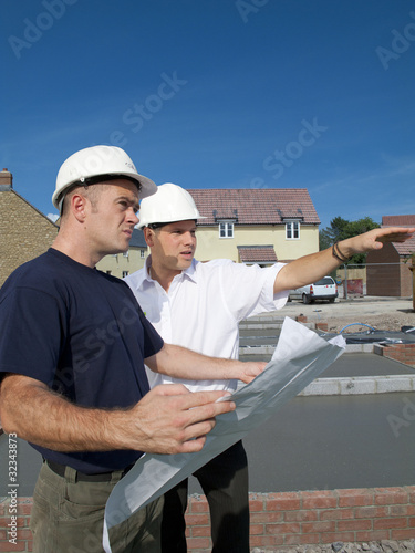 Foto: Construction workers holding blueprints talking on construction site Construction workers holding blueprints talking on construction site