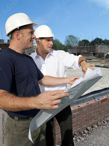 Photo: Construction workers holding blueprints talking on construction site Construction workers holding blueprints talking on construction site