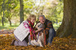 Happy senior couple sitting in autumn leaves petting dog