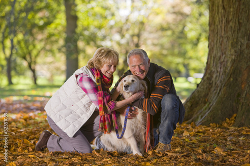 Photo: Happy senior couple sitting in autumn leaves petting dog Happy senior couple sitting in autumn leaves petting dog