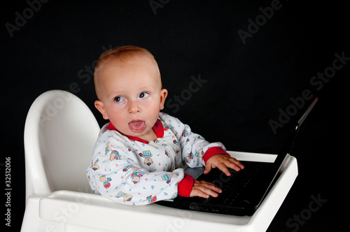Photo: Baby with the laptop on the black backround Baby with the laptop on the black backround