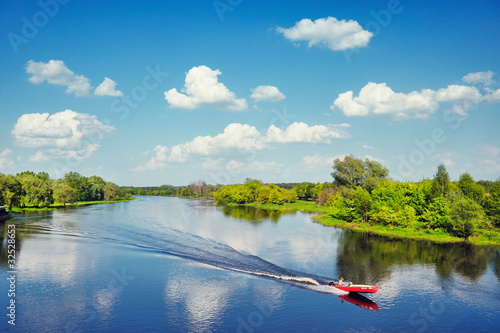 Fototapeta Landscape with a man and dog in a boat flowing by the river.