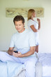 Man in bedroom holding cell phone with woman in background