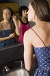 Two Young Women Looking At Themselves In A Bathroom Mirror