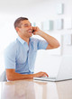 Young man talking on mobile while working on laptop
