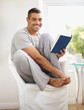 Foto: Smiling young man reading novel at home Smiling young man reading novel at home