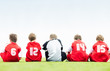Rear view of team players sitting in a line on field