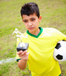 A kid looks at trophy while holding a football on field