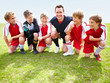 Coach with his soccer team kneeling in a row on field