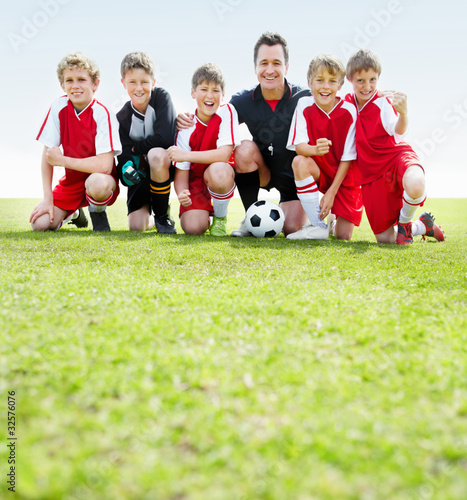 Photo: A coach and goal keeper sitting with team in a line on ground A coach and goal keeper sitting with team in a line on ground