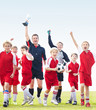 Happy coach with soccer team holding up trophy on field