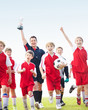 Excited soccer team with their coach holding up trophy on field