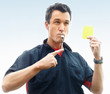 Soccer referee blowing whistle and pointing at a yellow card