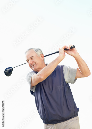 Foto: Sporty senior man swinging a golf club against clear sky Sporty senior man swinging a golf club against clear sky