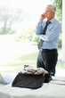 An elderly business man over cellphone with laptop and luggage
