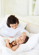 Sick boy lying in bed while his mother sitting beside him