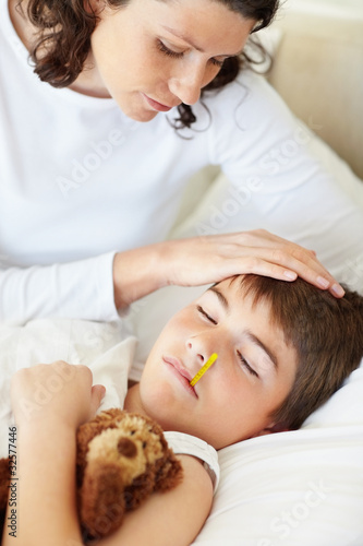 Foto: Sad mother checking temperature of her sick son with thermometer Sad mother checking temperature of her sick son with thermometer