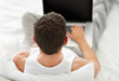 A young man working on his laptop while sitting in bed