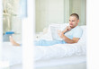 Photo: Happy middle aged male reading newspaper in bed at home Happy middle aged male reading newspaper in bed at home