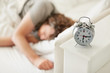 Closeup of table alarm clock with man sleeping at the back