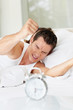Angry young man switching off the alarm clock in morning