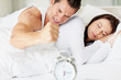Couple in bed and angry man switching off the alarm clock in mor
