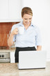 Cheerful executive using laptop while drinking tea in a kitchen