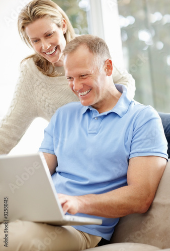 Photo: Happy middle aged couple working on a laptop at home Happy middle aged couple working on a laptop at home