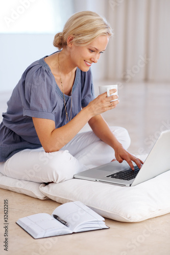 Photo: Beautiful young woman using laptop holding a coffee cup Beautiful young woman using laptop holding a coffee cup