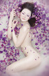 Attractive naked girl enjoys a bath with milk and rose petals.