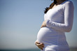 A pregnant woman standing on the beach, holding her belly