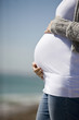 A pregnant woman standing on the beach, holding her belly