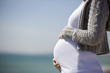 A pregnant woman standing on the beach, holding her belly