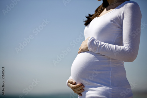 Photo : A pregnant woman standing on the beach, holding her belly A pregnant woman standing on the beach, holding her belly